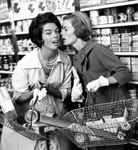 Two women whisper to each other in aisle of shop 9th September 1960.