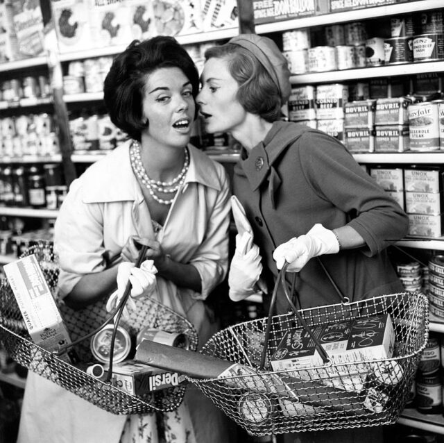 Two women whisper to each other in aisle of shop 9th September 1960.