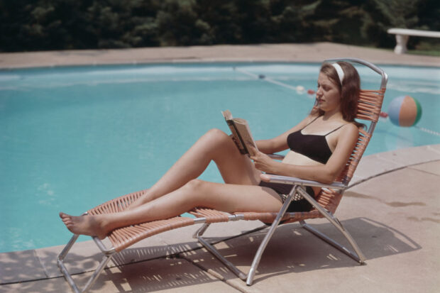 Woman reading book on lounge chair at pool