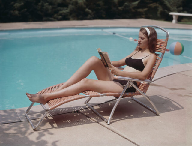 Woman reading book on lounge chair at pool