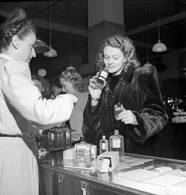 Shopping in the 1940s. A young woman in a perfume store where a sales woman is presenting some of the ...